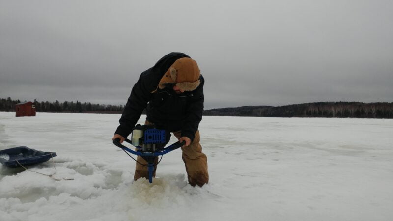 WJ14 7537 Man drilling hole in the ice wearing Tough Duck 3 in 1 parka and insulated bib overall